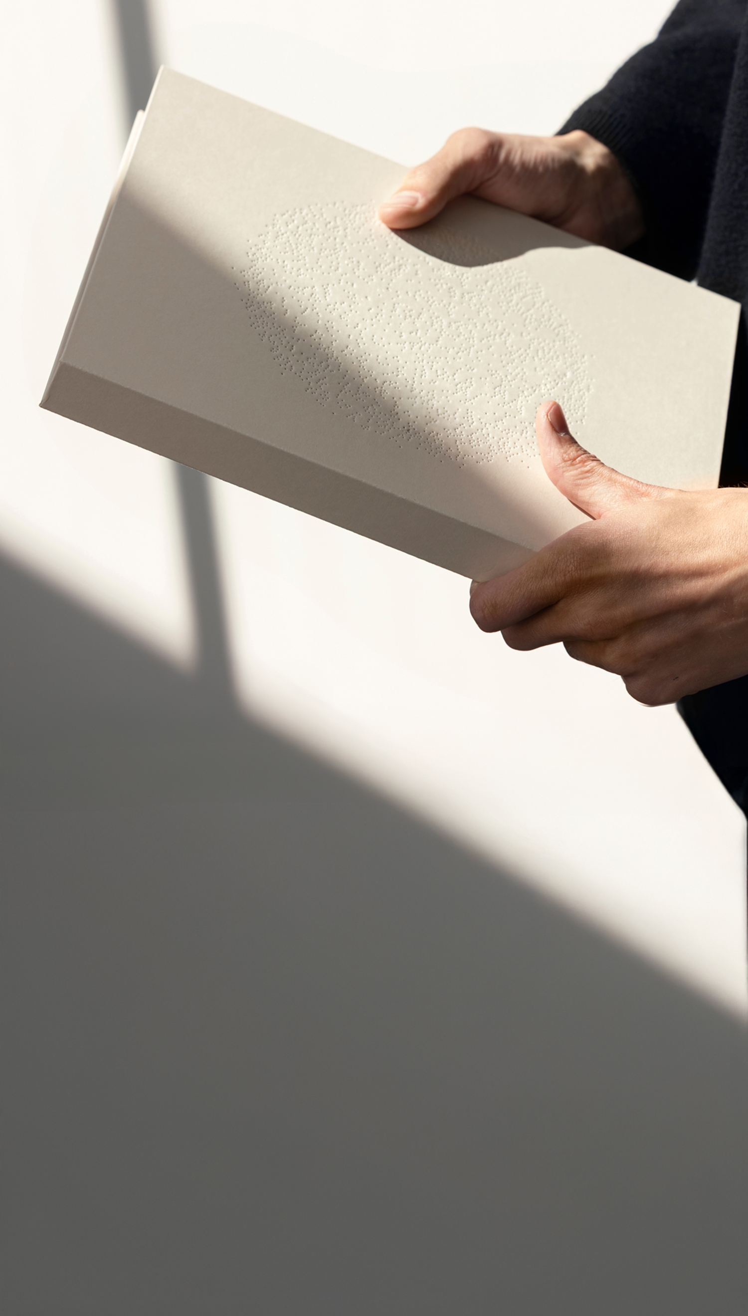 Person holding a closed beige book with embossed texture, against a light background with shadow.